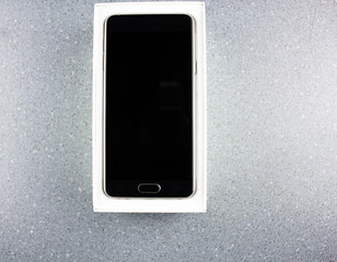 Smartphone in a box. Modern new black smartphone in a white box on a blue background close-up. New gadget, gift, choice, order.