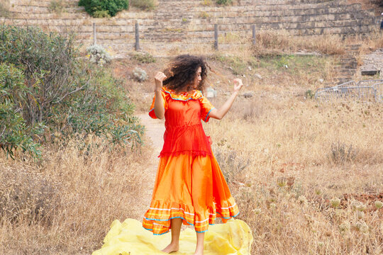 Girl with curly hair wearing orange dress standing on yellow tissue