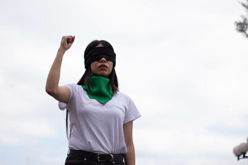 young millennial girl protesting for women's rights at a blindfolded rally with green bandana
