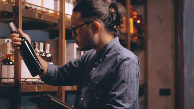 Young Asian sommelier is checking the drink store. A bartender wearing glasses and hair tie Wine stands to check the drink list and prepares to serve drinks to customers at the hotel bar.