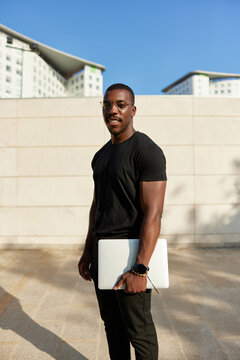 Smiling black guy with laptop standing on street