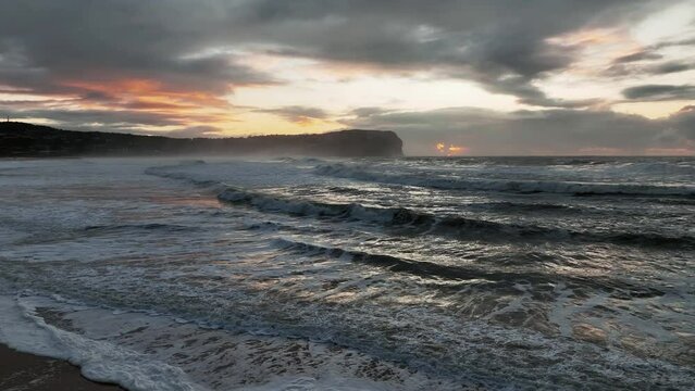 Aerial sunrise seascape with 8 to 13ft waves and rain clouds at MacMasters Beach on the Central Coast, NSW, Australia.