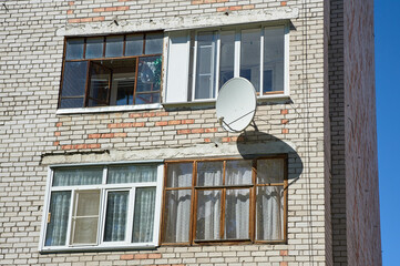 A satellite dish is hanging on the wall of a brick house