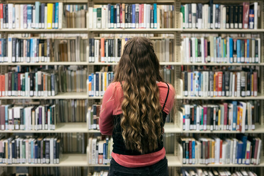 Student Looking At Bookshelves In Library