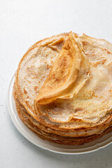 Stack of French crepes or traditional Russian blini on white plate on light background. Thin pancakes made from butter, eggs and milk. Traditional festival meal of Maslenitsa.