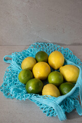 Blue mesh eco bag with fresh lemons and limes on a light stone background. Front view