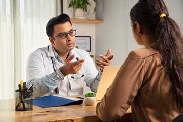 Asian Indian man or male physician or doctor sitting in a modern clinic wearing a stethoscope and...
