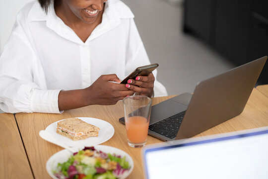 Faceless black woman browsing smartphone near laptop
