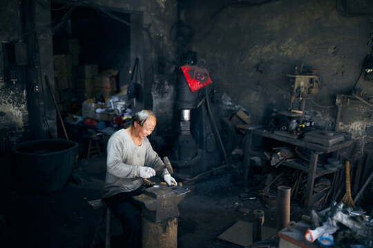 An East Asian Ironworker manufactures a Chinese kitchen knife.