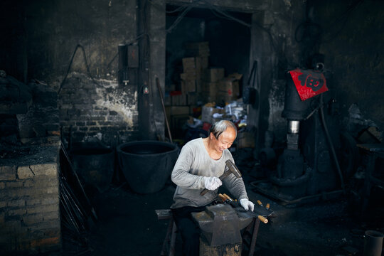 An East Asian Ironworker manufactures a Chinese kitchen knife.