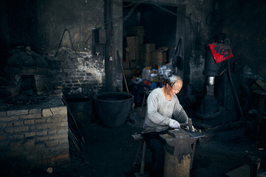 An East Asian Ironworker manufactures a Chinese kitchen knife.