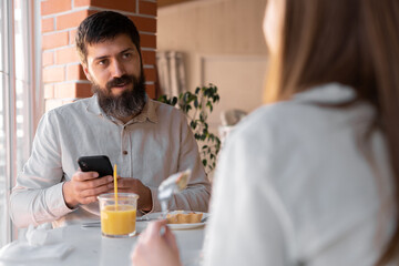 Happy young couple having breakfast in cafe, enjoying together using cell phone. Cafe or restaurant interior.