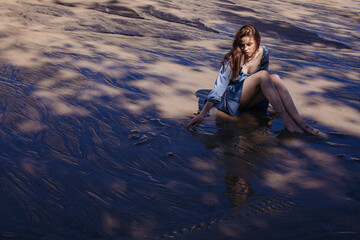 Pensive woman posing at nature and touching wet sand