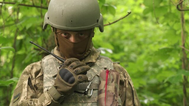 a portrait of a Ukrainian military man communicating by radio. a military man in the forest reports news on a walkie-talkie and gives orders. communication between units during a combat mission