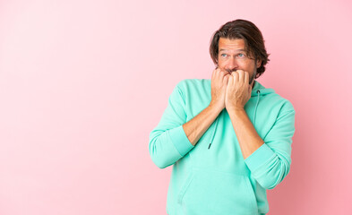 Senior dutch man isolated on pink background nervous and scared putting hands to mouth
