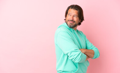 Senior dutch man isolated on pink background with arms crossed and happy