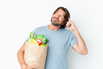 Senior dutch man holding grocery shopping bag over isolated background having doubts and thinking