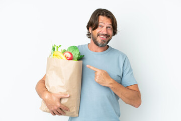 Senior dutch man holding grocery shopping bag over isolated background pointing to the side to present a product