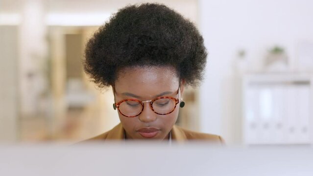 Busy Teacher Working On A Computer Inside And Looking Focused. Face Of Young Education Worker With Afro And Glasses Typing Assignment Or Grading Test Papers Online At A Desk Inside A Modern Campus.