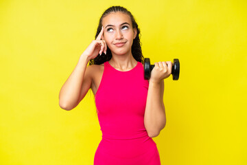 Young sport woman making weightlifting isolated on yellow background having doubts and thinking
