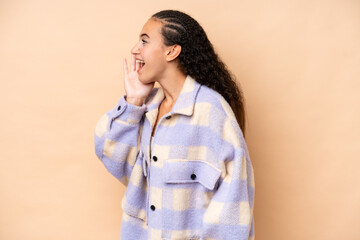 Young woman isolated on beige background shouting with mouth wide open to the side
