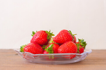 Many red strawberries on glass plate and wooden table top view