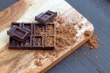 Chocolate bar with scattered cocoa powder on the wooden board.