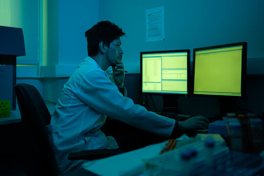 Scientist Working In A Blueish Laboratory Next To The Computer.