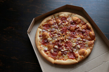 Pizza in a cardboard box against a dark background. View from above. Pizza delivery.