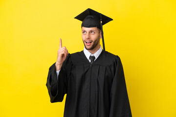 Young university graduate caucasian man isolated on yellow background pointing up and surprised