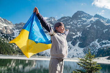 Boy with Ukrainian flag is standing on the shore of a lake. Morskie Oko
