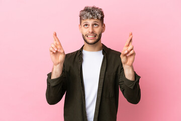 Young handsome caucasian man isolated on pink background with fingers crossing and wishing the best