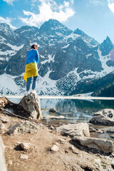 A woman with Ukrainian flag is standing on the shore of a lake. Morskie Oko