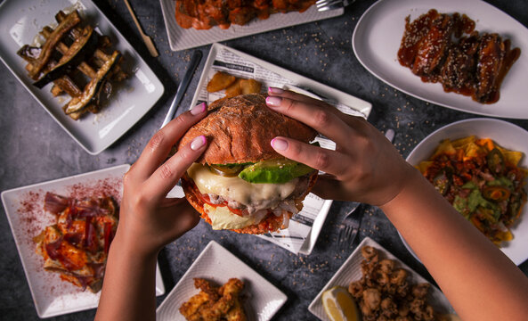 Woman's Hands Holding Tasty American Burger And French Fries At Restaurant Table. Flat Lay. Top View