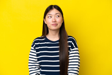 Young Chinese woman isolated on yellow background having doubts while looking up