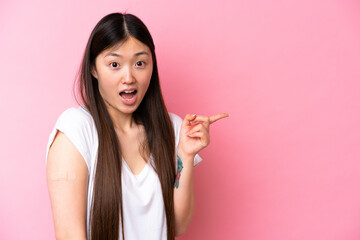 Young Chinese woman wearing a band aids isolated on pink background surprised and pointing finger to the side