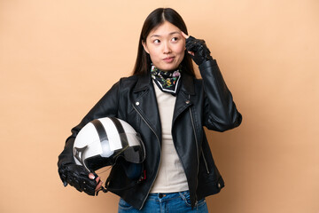 Young Chinese woman with a motorcycle helmet isolated on beige background having doubts and thinking
