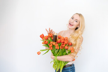 Studio portrait gorgeous blonde woman with long wavy hair holding bouquet red tulip flowers holds a bottle of shampoo in her hand. White isolated background, copy space, close-up.