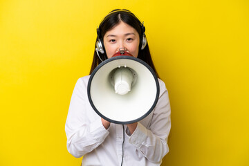 Telemarketer Chinese woman working with a headset isolated on yellow background shouting through a megaphone