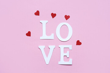 Word love from paper letters and red hearts on a pink background. Flat lay, place for text. Valentine's day background.