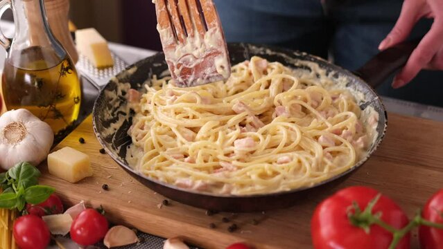 making pasta carbonara - mixing spaghetti and sauce made of cream and chopped pancetta bacon in frying pan