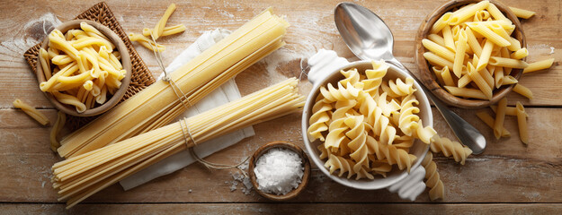Raw pasta: fusilli, penne, casarecce, spaghetti and tagliatelle on floured rustic wooden background, top view.
