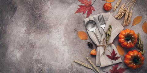 Thanksgiving autumn place setting with cutlery, decorative pumpkins and colorful leaves. Top view, flat lay. Banner. Selective focus.