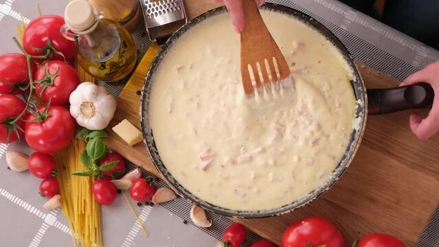 making pasta carbonara - mixing sauce made of cream and chopped pancetta bacon in frying pan