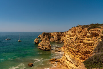 View of the cliffs by Praia de Marinha. Arco natural. In the distance, on the ocean, a catamaran and a yacht. Lagoa, Algarve, Portugal