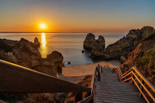 Sunrise on the coast of Lagos. View from Praia do Camilo of the ocean and sky. On the sides there are cliffs and wooden stairs that lead to the beach. Lagos, Portugal.