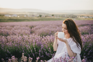 Young beautiful woman in white dress drinking herbal tea in lavender field.