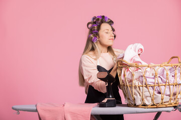 Smiling happy woman in pink background sniffs clean washed laundry smelling of powder freshness,...