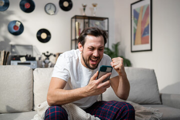 A satisfied guy shouts loudly into his phone he is very happy at the thought of his favorite team winning. Watching the match alone in the living room.