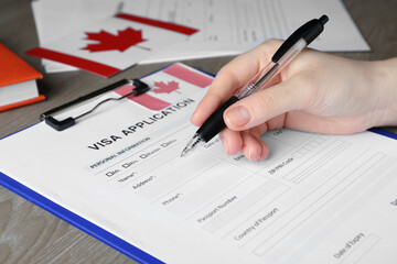 Woman filling visa application form to Canada at table, closeup